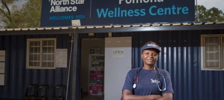 A woman with a stethoscope stands in front of a blue box clinic that says "North Star Alliance welcomes you" and "Pomona Wellness Centre"